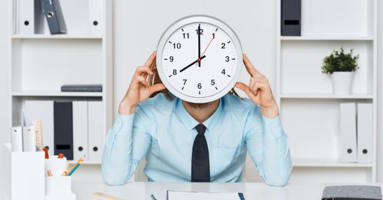 Une personne assise derrière son bureau tient une horloge devant son visage.